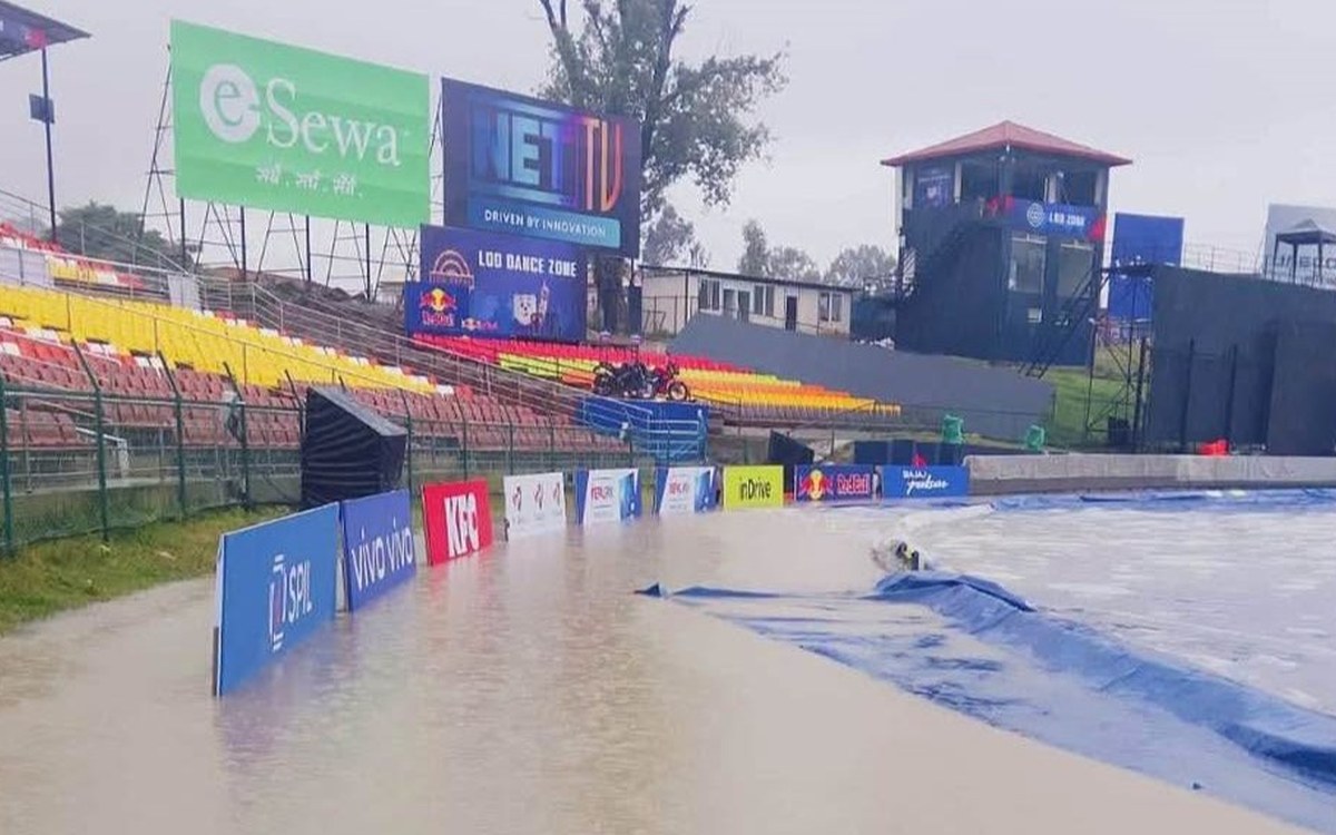 Rain covers spread over a wet TU Ground outfield at Kirtipur with empty stands and venue boards in the background