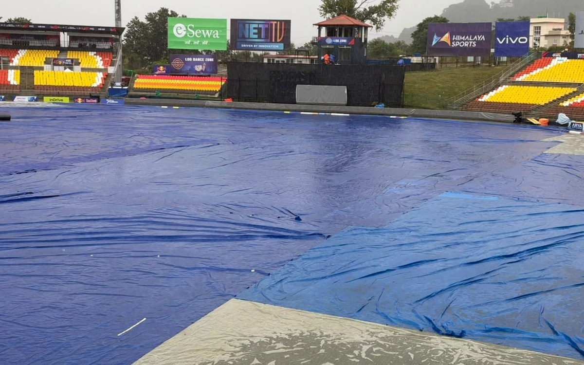 The TU Ground in Kirtipur under blue rain covers with empty yellow and red stands behind it on a rainy day